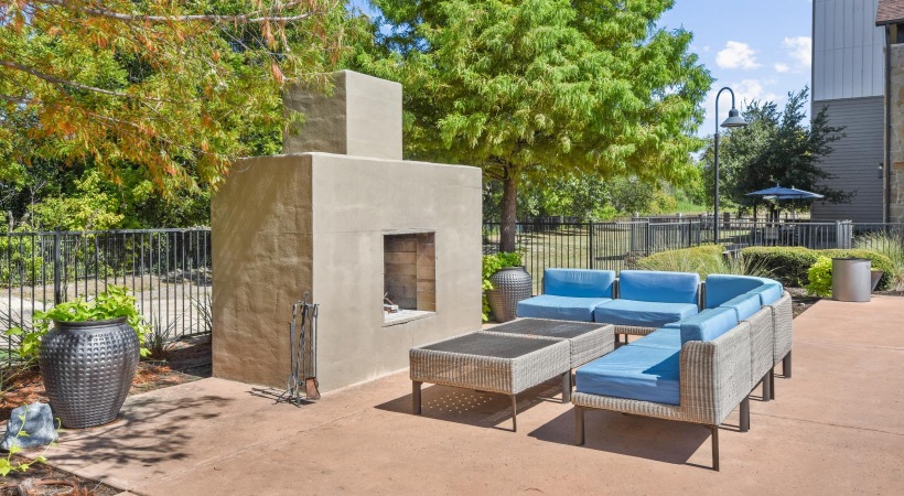 a patio with blue chairs and a stone structure with trees and a fence