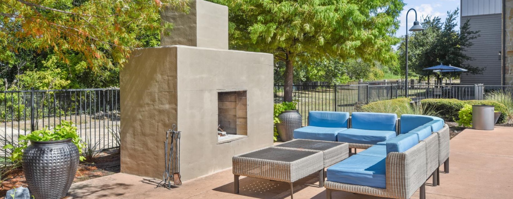 a patio with blue chairs and a stone structure with trees and a fence
